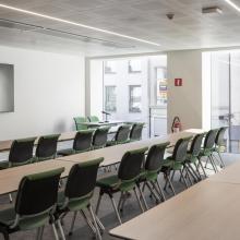 Whatsup: vergaderruimte met tafels, groene stoelen en presentatiescherm